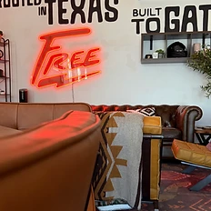 Yellow leather chair with a Southwestern throw blanket beneath the Rooted in Texas Built to Gather mural and FREE neon sign