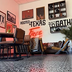 Leather lounge chairs and sofa under the Rooted in Texas Built to Gather wall with the glowing FREE neon sign