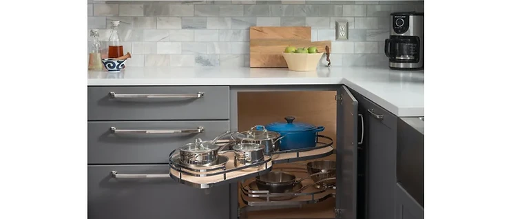 Corner cabinet with kidney-shaped pull-out shelf system storing cookware and a blue dutch oven