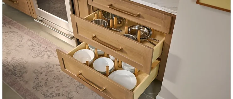 Kitchen drawers with wooden pegboard organizers holding stainless steel pots and stacked ceramic dinnerware
