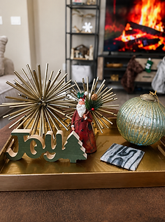Holiday vignette on a gold tray with a JOY sign, starburst ornament, and Santa figurine