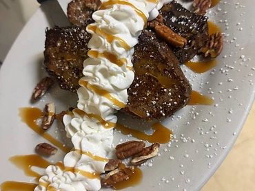 French toast with whipped cream, pecans, powdered sugar, and caramel drizzle