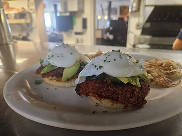 Two poached egg and avocado breakfast plates with hash browns and restaurant kitchen background