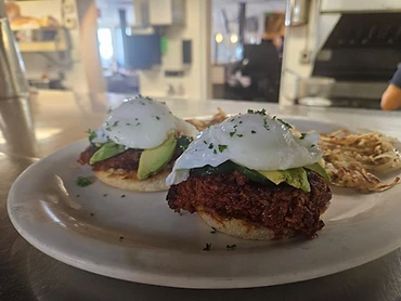 Two poached egg and avocado breakfast plates with hash browns and restaurant kitchen background