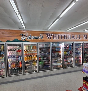 Refrigerated dairy and beverage cases beneath a Welcome to Whitehall Market mural