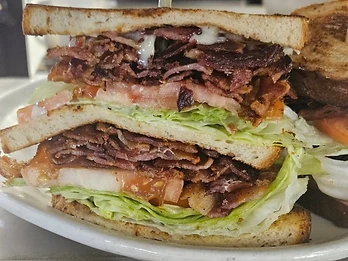 Tall stacked sandwich with sliced meat, lettuce, tomato, and toasted bread