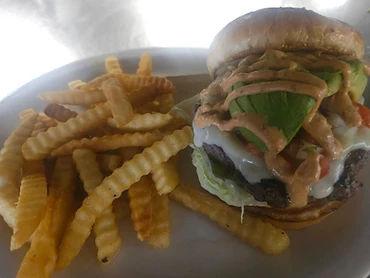 Burger with avocado and green toppings served with crinkle-cut fries