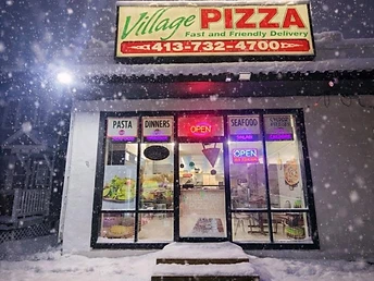 Village Pizza storefront during snowfall