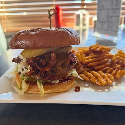 A tall burger served with waffle fries on a white plate