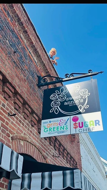 Brick storefront with the Sweet Annie’s, Grits & Greens Market, and Sugar Chef hanging sign