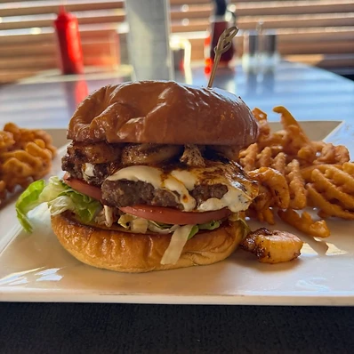 A burger with tomato and lettuce served with waffle fries