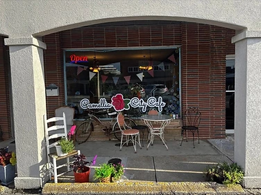 Camellia City Cafe storefront with window lettering, rose logo, outdoor tables, Open sign, and entrance