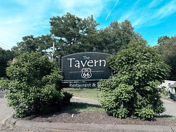 The Tavern on 66 roadside sign surrounded by green shrubs in East Hampton, Connecticut