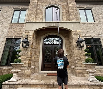 Technician cleaning a large arched window on a stone estate