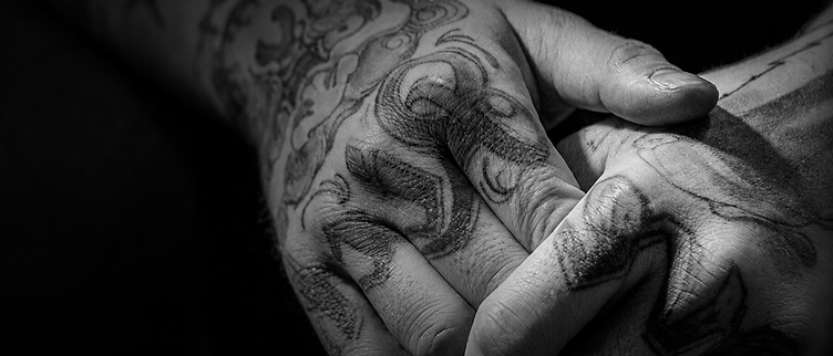 Tattooed hands resting together in a gesture of reflection