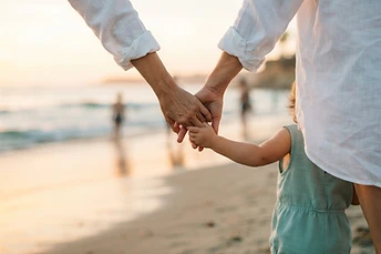 A mother's hand gently holding her child's hand in golden hour light