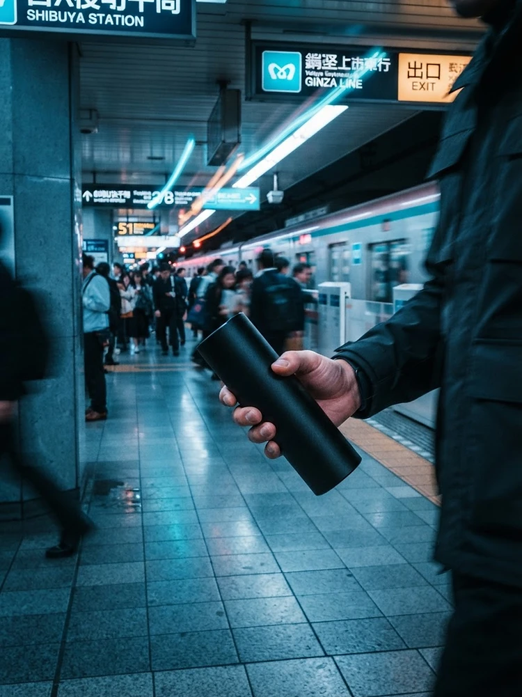 Hand holding a sleek power bank in a neon-lit transit station