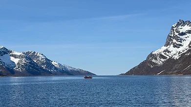 Fishing boat on a calm Arctic fjord surrounded by snow-capped mountains at Ersfjordbotn