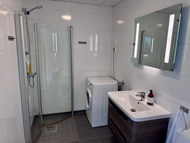 Modern bathroom with walk-in shower, washing machine and LED-lit vanity in a fjordside apartment