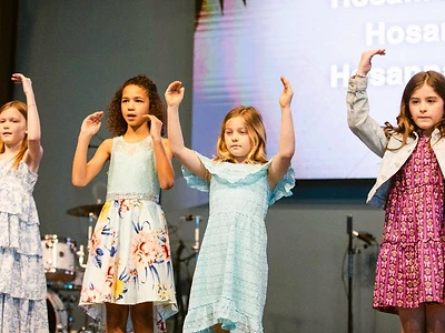 Four young girls raise their hands in worship on stage