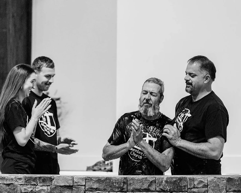 A man is baptized as friends applaud beside the baptistry at Abundant Life Church