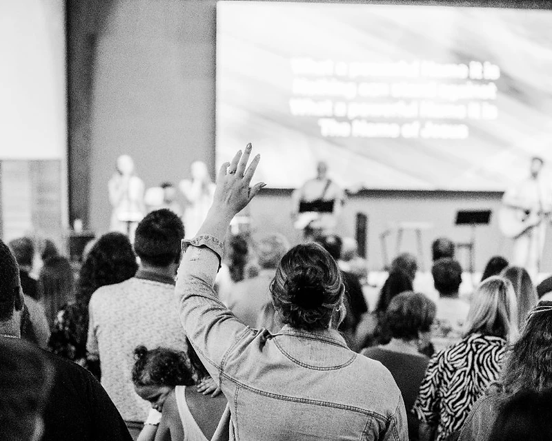 A woman lifts her hand in worship among the congregation as the band leads from the stage