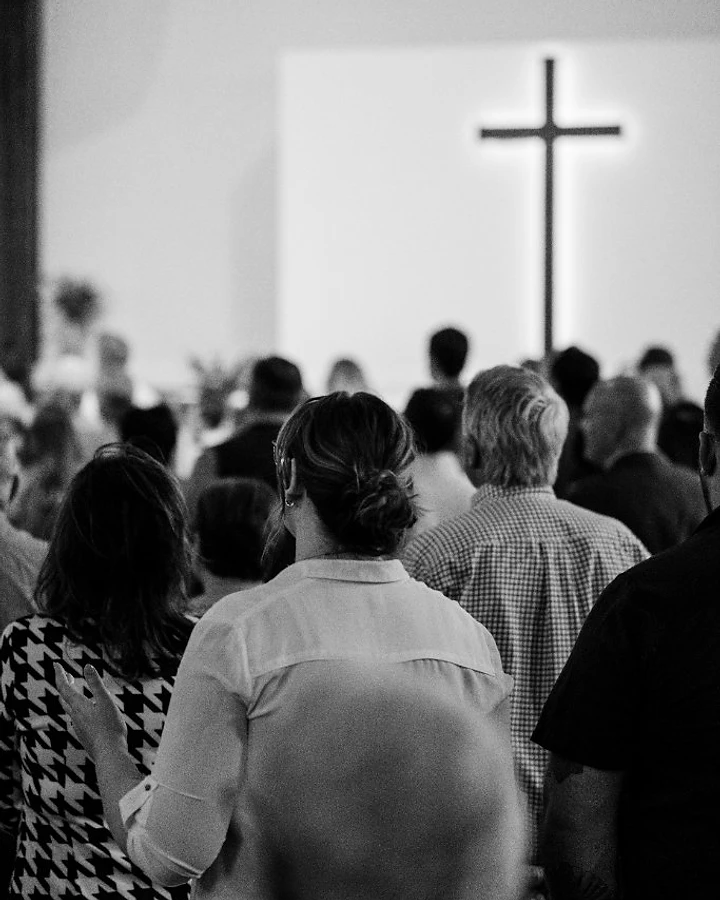 The congregation faces a glowing cross on the stage during a Sunday worship service