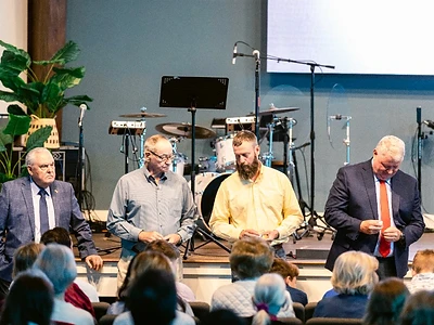 Four men stand together on stage leading a Sunday service