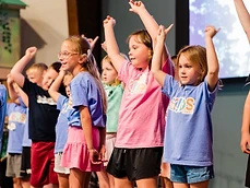 LifeKIDS children raise their hands and sing on stage during kids worship