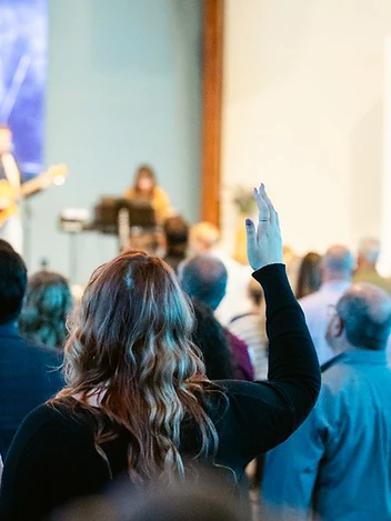 A woman raises her hand in worship as the band leads the congregation