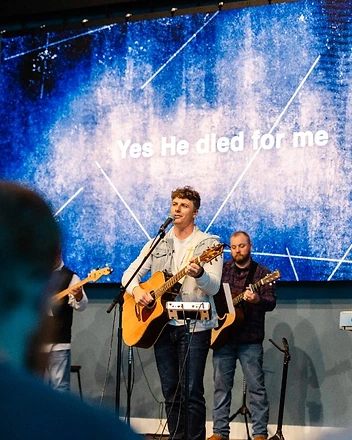 A worship leader sings and plays guitar with the band during a Sunday service