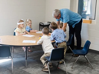 A caring volunteer helps preschoolers with an activity in a bright, safe classroom