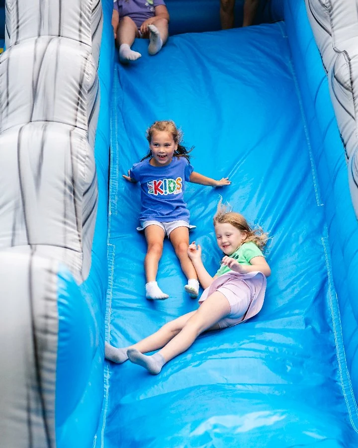 Two LifeKIDS girls laugh as they slide down an inflatable water slide at a church event