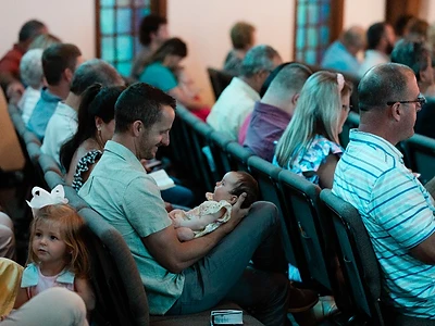 A dad smiles down at his newborn while families sit together during a Sunday service