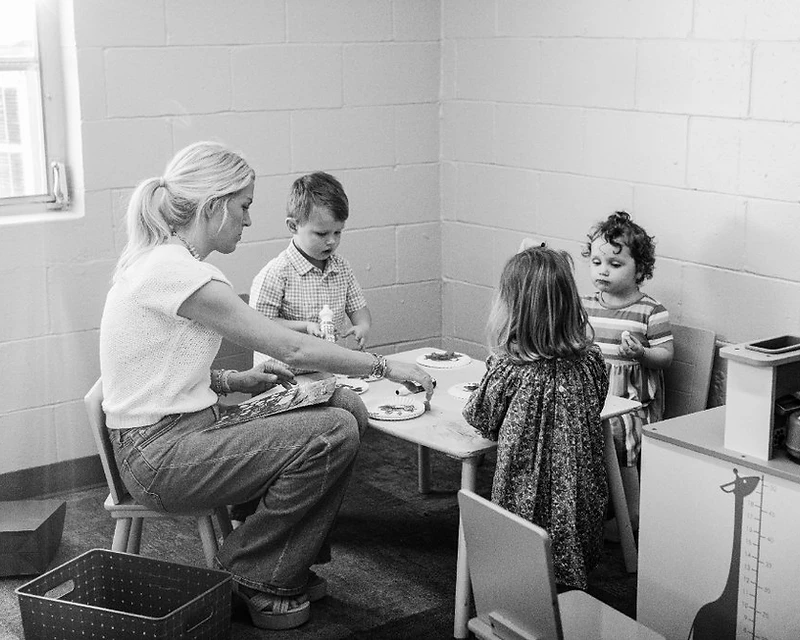 A volunteer works on a craft with little ones at a table in the nursery classroom