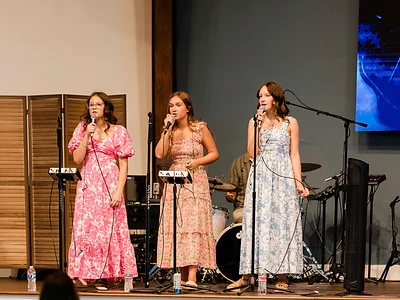Three women sing together on stage during a Sunday worship service