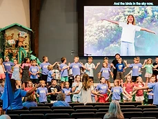 Dozens of LifeKIDS children sing and do hand motions on stage during a VBS celebration