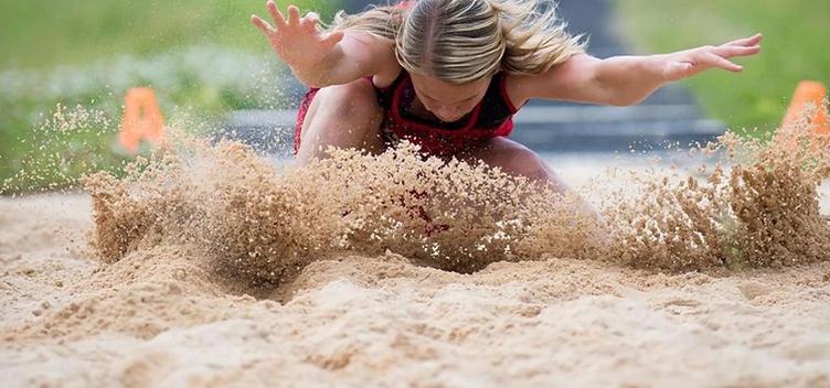 Cherokee Junior Warriors athlete landing in the long jump pit