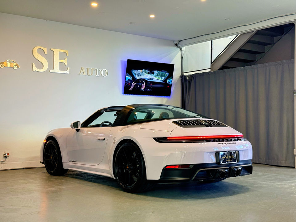 White Porsche 911 Targa 4 GTS, three-quarter rear view from the driver side, in a dealer’s showroom.