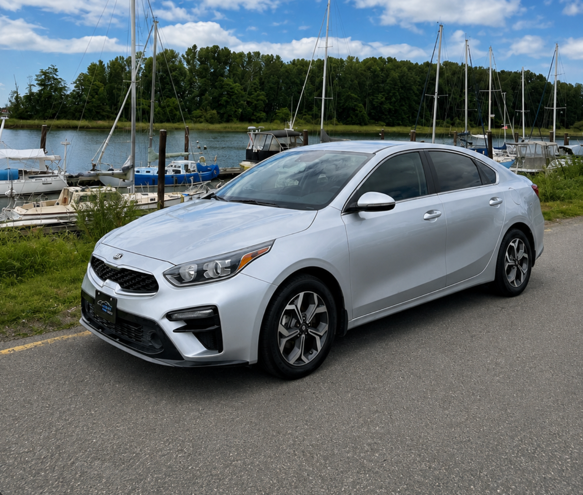 Silver Kia sedan, three-quarter front view, parked at a marina.