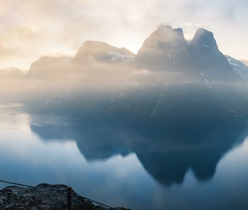Misty Norwegian fjords at dawn with a solitary figure on a distant cliff