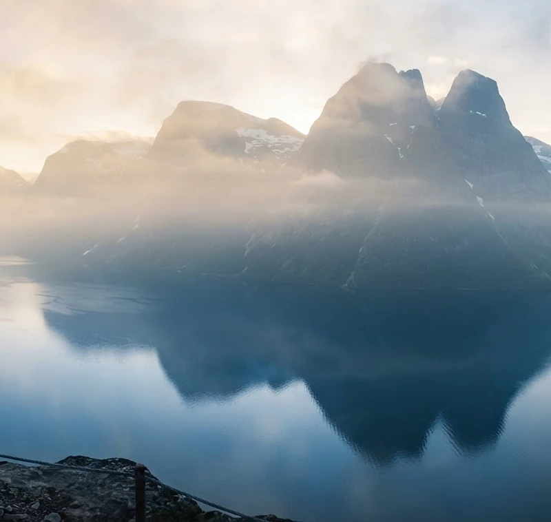 Misty Norwegian fjords at dawn with a solitary figure on a distant cliff