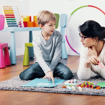 A psychologist and child engaging together on a playroom rug
