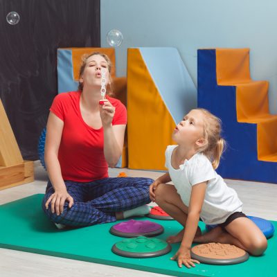 An occupational therapist blowing bubbles with a child on a therapy mat