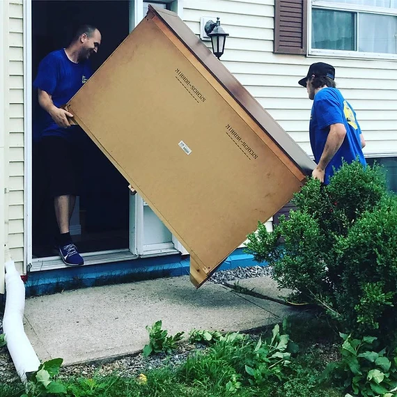YCML movers in matching blue shirts carrying a dresser out of a home