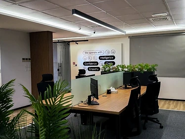Unifonic Offices in Amman with open timber workstations, glass meeting rooms, linear lighting, black ergonomic seating, and integrated green planting
