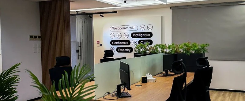 Unifonic Offices in Amman with open timber workstations, glass meeting rooms, linear lighting, black ergonomic seating, and integrated green planting