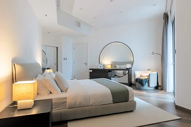 Primary bedroom, flat interior design, Amman: bouclé armchair, round mirror console, layered bedding