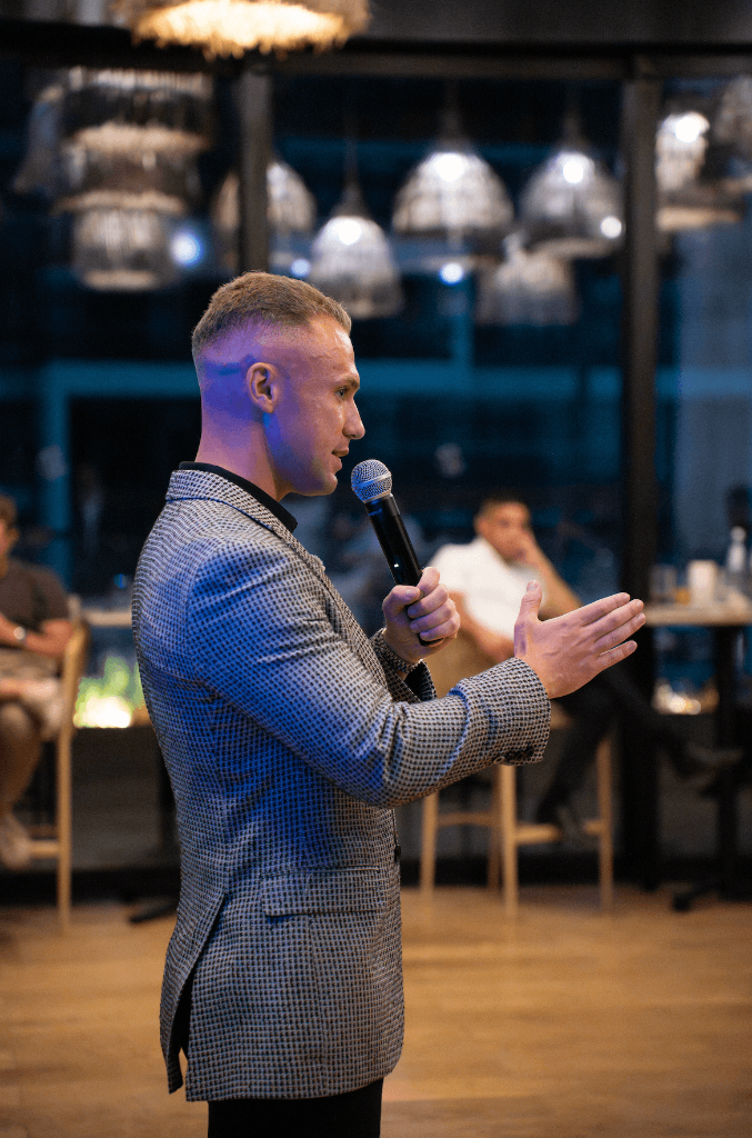 James Demetriades speaking with a microphone at a private Commerce Club event