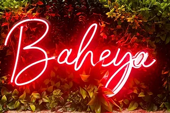 Baheya neon sign glowing against a wall of foliage